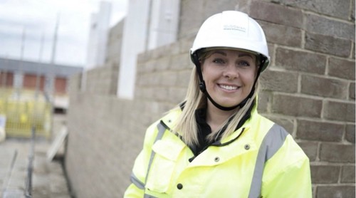 Amy McCreesh wearing a hard hat and high visibility jacket in front of a semi-constructed home