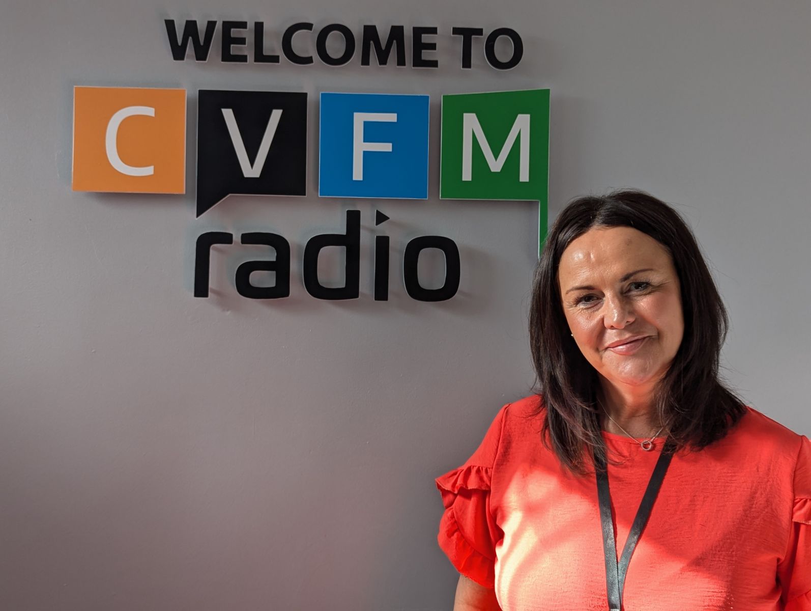 women with dark shoulder length hair and wearing a bright fuscia short sleeved top in front of a grey wall which says welcome to CVFM